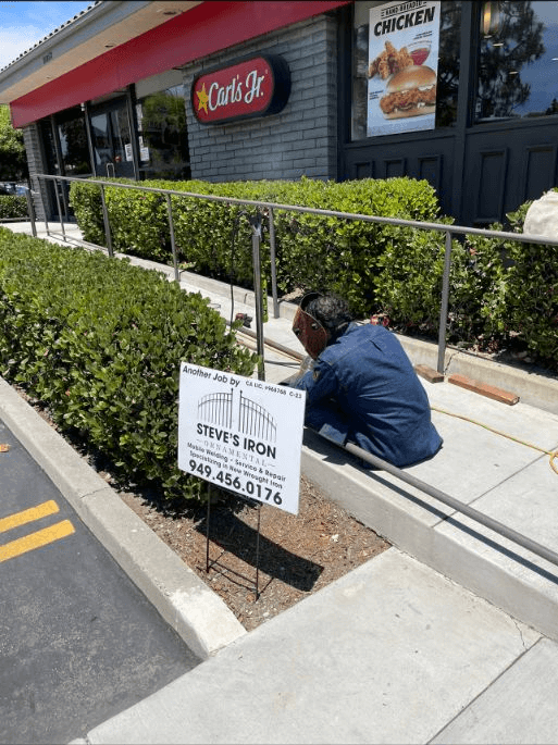 A man kneeling down next to bushes on the side of a road.