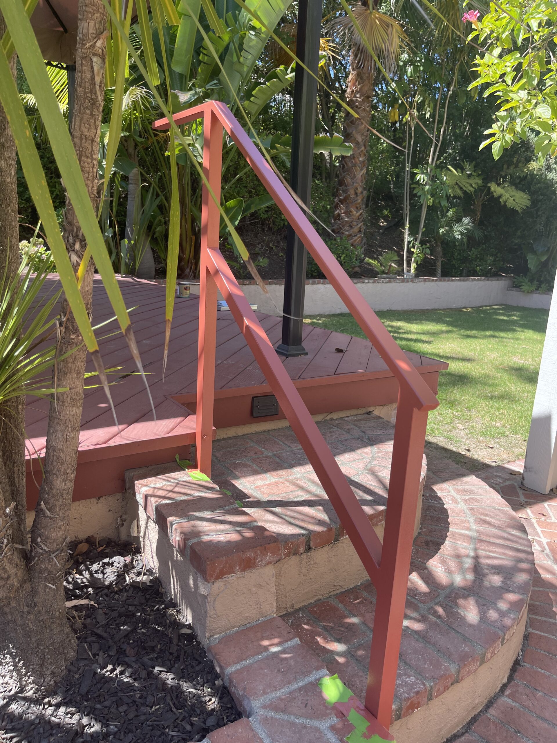 Red railing on brick steps, garden background.