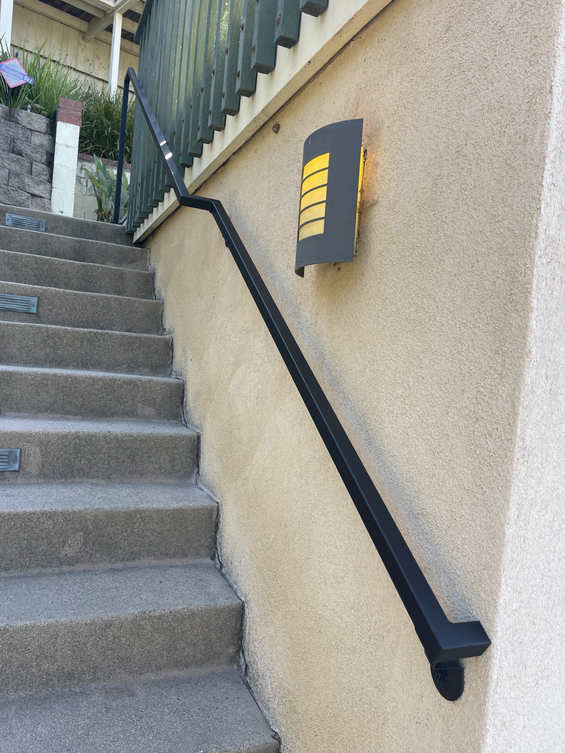 Staircase with black handrail and wall light.